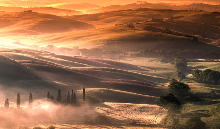 Sunrise over rolling hills in Tuscany, Italy, with misty valleys and warm golden light, captured in a stunning landscape photography HD wallpaper.