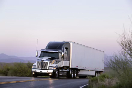 HD desktop wallpaper featuring a Western Star vehicle driving on a desert road at dawn with mountains and sparse vegetation in the background.