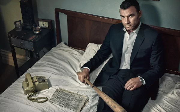 HD wallpaper featuring a serious man from 'Ray Donovan' seated on a bed with a baseball bat, newspaper, and old phone.