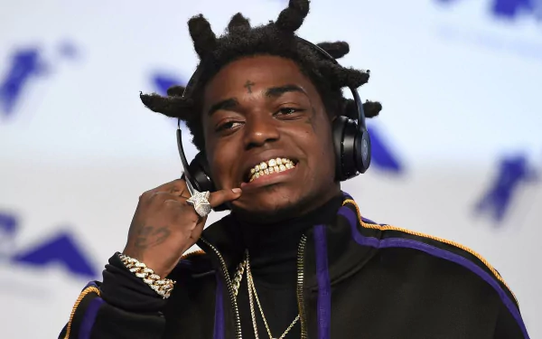 HD desktop wallpaper featuring a smiling person with distinctive hair, gold teeth, and headphones, tagged with Kodak Black, on a blurred background.