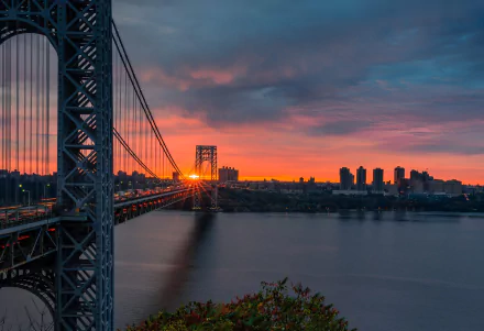 Sunset over the George Washington Bridge spanning the river in New York, USA, with vibrant orange and blue hues reflecting on the water.