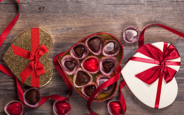 4K Ultra HD wallpaper featuring heart-shaped chocolates in decorative boxes with red ribbons, evoking a romantic Valentine's Day holiday theme.