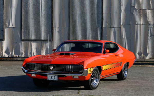 Bright orange 1970 Ford Torino vehicle parked in front of corrugated metal wall — high-resolution 4K Ultra HD PC desktop wallpaper and background.