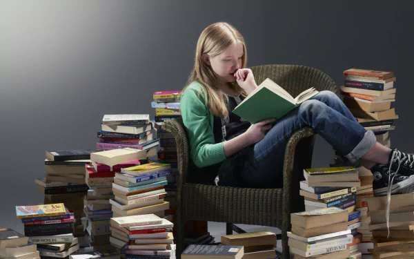 A child sits in a cozy armchair, engrossed in a book, surrounded by stacks of books, creating a warm atmosphere for reading. This HD photography captures the joy of literature.