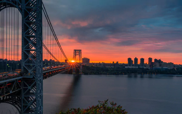 Sunset over the George Washington Bridge spanning the river in New York, USA, with vibrant orange and blue hues reflecting on the water.