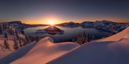 Snow-covered landscape at Crater Lake, Oregon, during winter sunrise. The serene lake is surrounded by a snowy island and mountain scenery, capturing the beauty of nature in this HD wallpaper background.