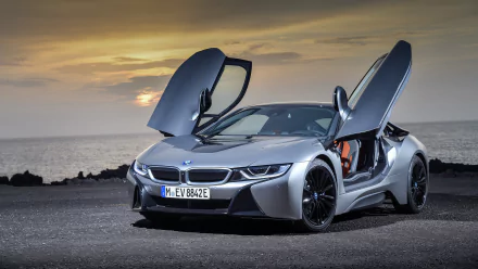 Silver BMW i8 supercar with butterfly doors open, parked by the sea at sunset, captured in 4K Ultra HD as a high-resolution PC desktop wallpaper.