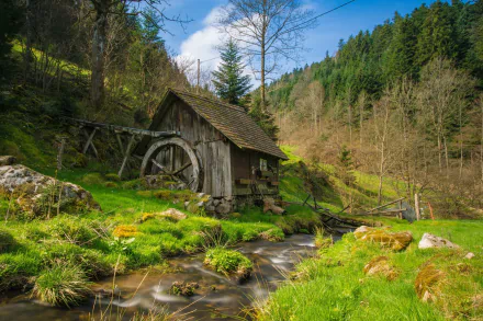 HD desktop wallpaper featuring a serene scene with a rustic watermill by a stream, surrounded by green grass and trees on a hillside.