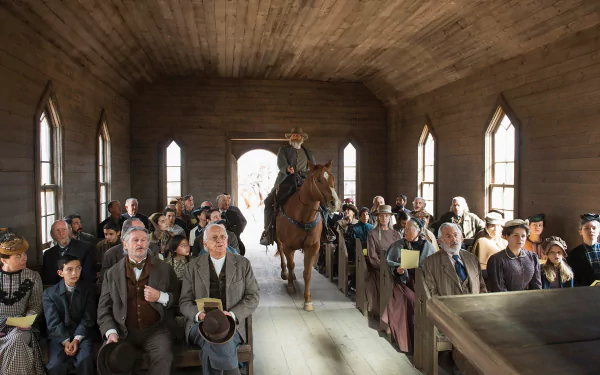 HD desktop wallpaper from Godless featuring a person on horseback inside a wooden building surrounded by a crowd of onlookers.