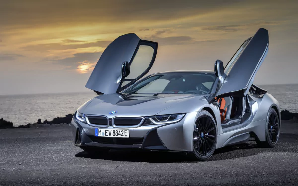 Silver BMW i8 supercar with butterfly doors open, parked by the sea at sunset, captured in 4K Ultra HD as a high-resolution PC desktop wallpaper.