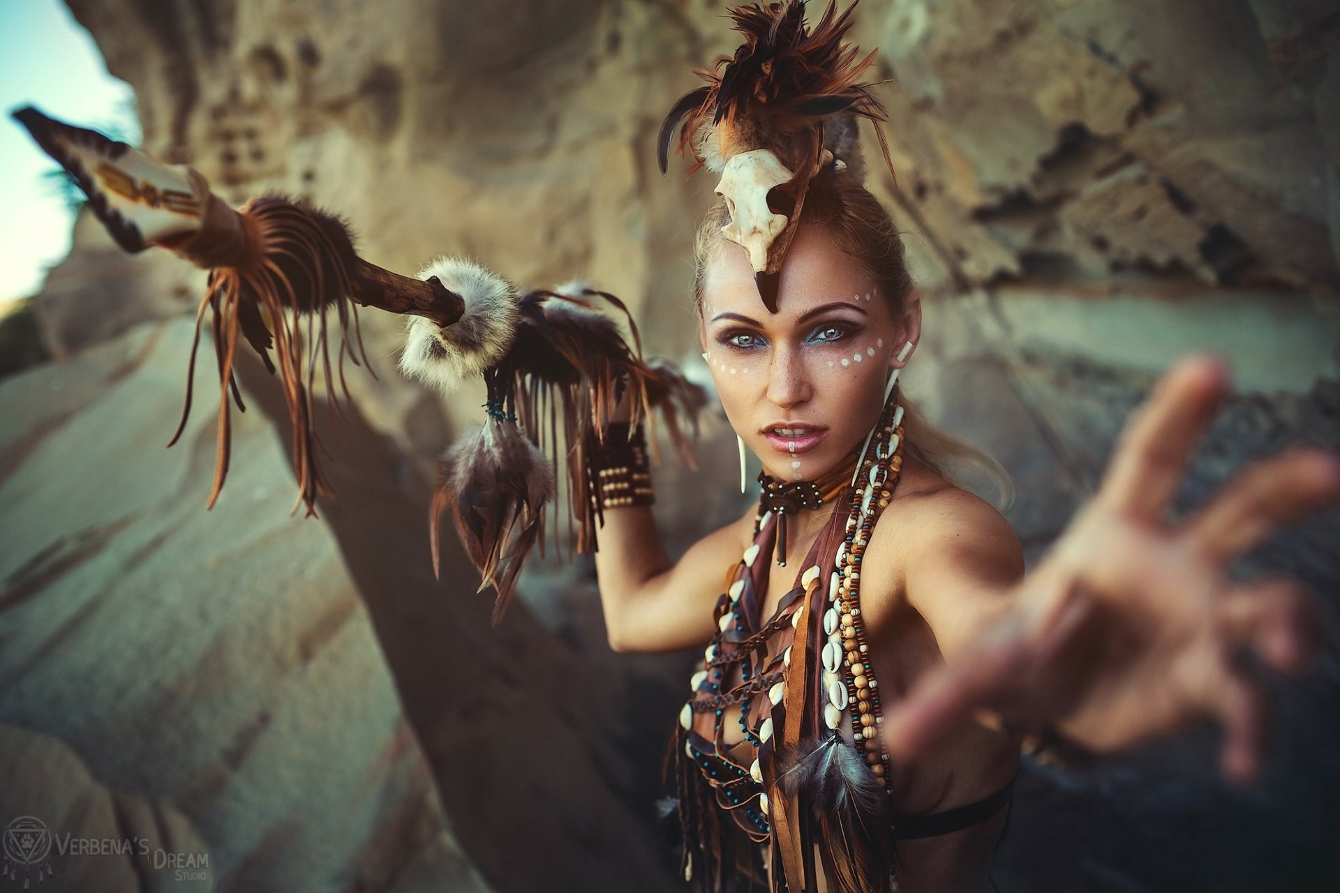 HD PC desktop wallpaper featuring a woman in detailed cosplay with tribal-inspired accessories and an intense expression against a natural rocky background.