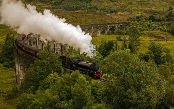 A vintage steam locomotive emitting thick white smoke crosses a curved viaduct surrounded by lush greenery in this HD PC desktop wallpaper.