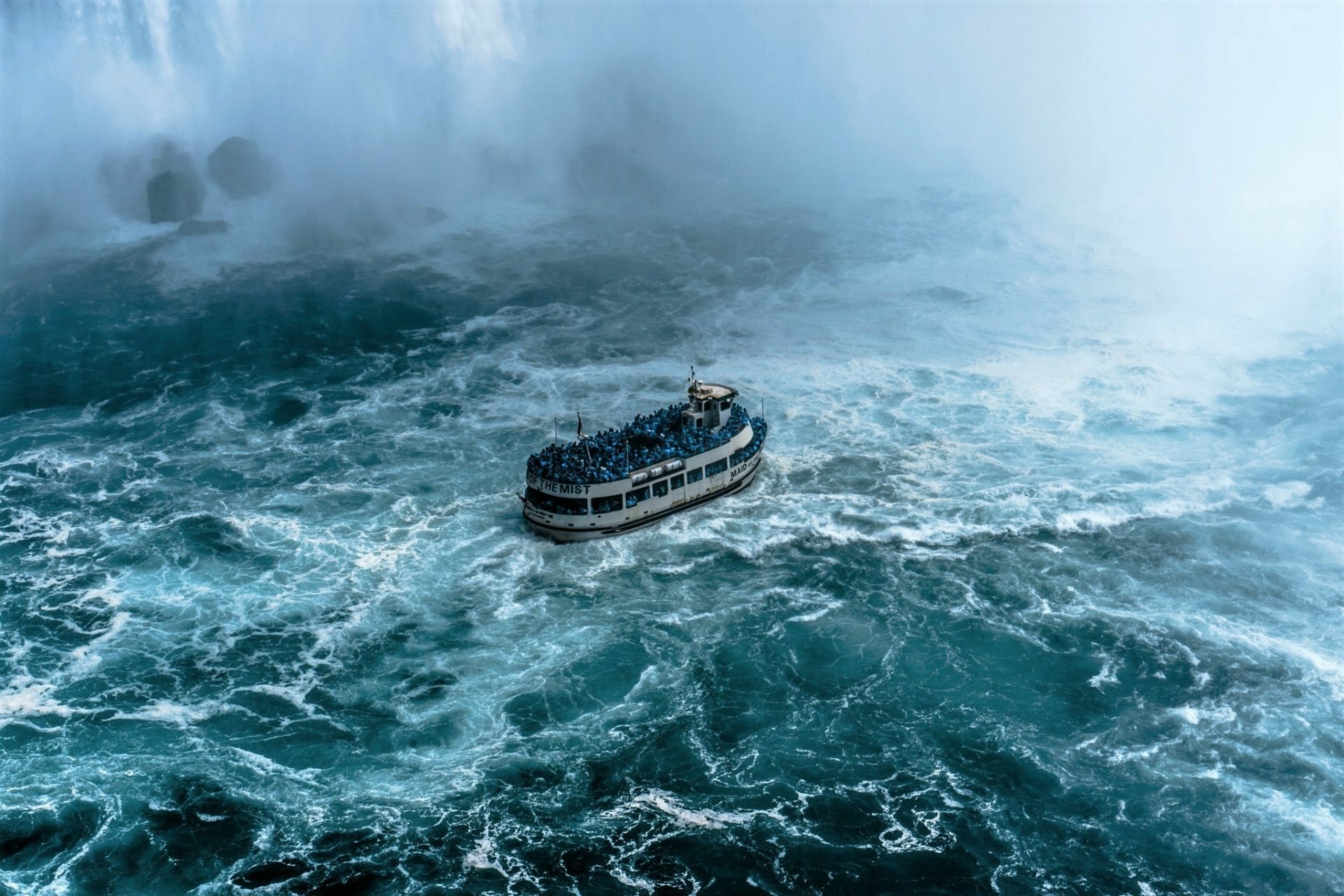 HD PC desktop wallpaper: a tour boat (vehicle) cutting through churning turquoise waters beneath Niagara Falls, mist rising around the vessel.