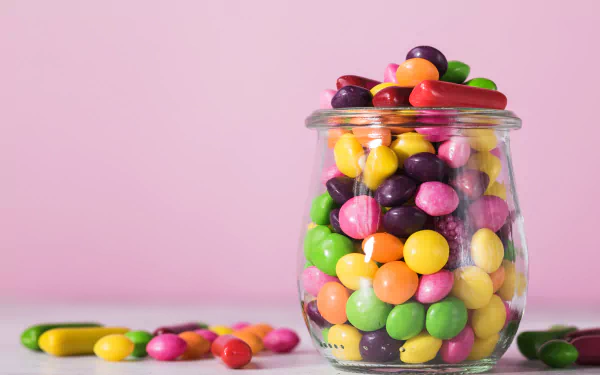 A 4K Ultra HD desktop wallpaper featuring a glass jar filled with colorful candy sweets against a soft pink background.