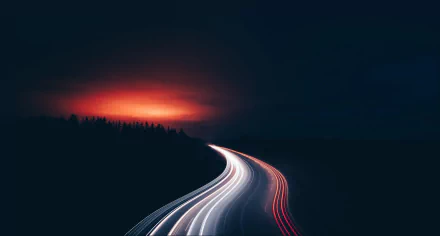 HD desktop wallpaper depicting a highway at night with light trails from vehicles. The sky glows with a reddish hue, highlighting the serene yet dynamic scene captured in this stunning time-lapse photography.