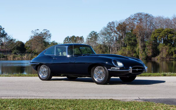 Black Jaguar E-Type parked by a lakeside road with trees and clear sky in the background, captured in HD for a PC desktop wallpaper.