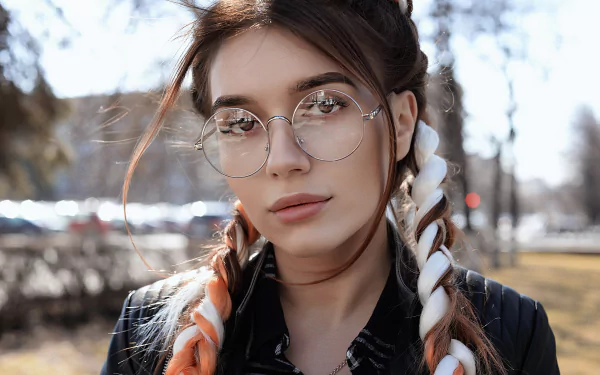 A confident brunette woman with hazel eyes and glasses, showcasing her unique style with braided hair. The image serves as a vibrant HD desktop wallpaper for fans of singers and models.
