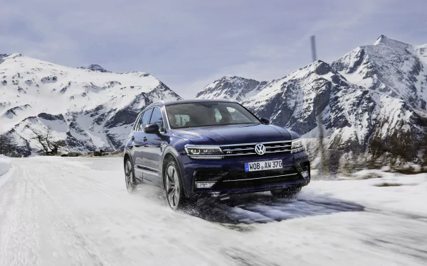 Volkswagen Tiguan SUV driving on a snowy mountain road with snow-covered peaks in the background, captured in 4K Ultra HD for a PC desktop wallpaper.