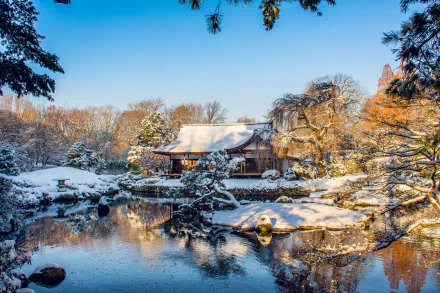 HD desktop wallpaper of a serene winter scene in Japan, featuring a traditional building beside a snow-covered lake in a park.