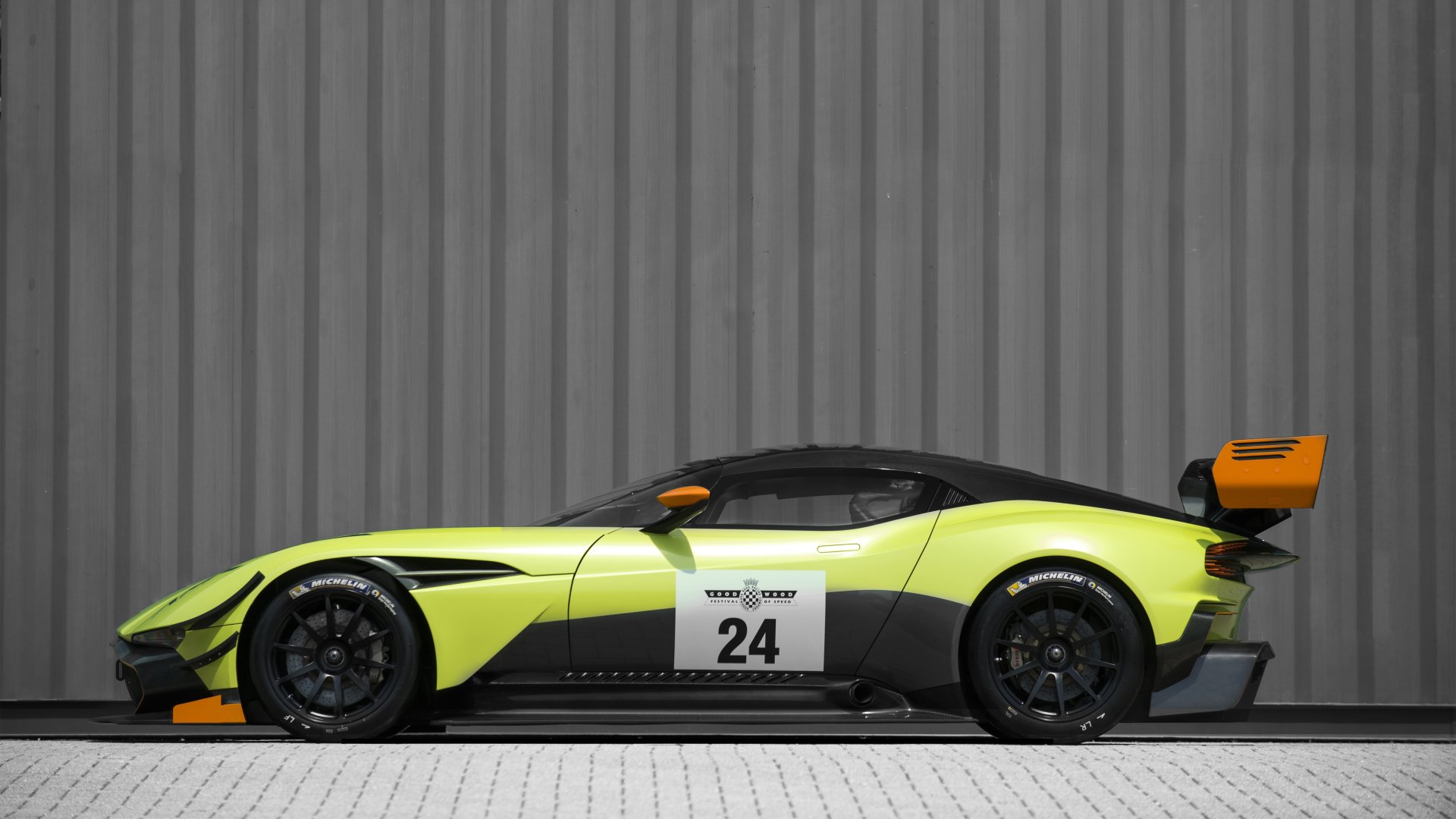 Aston Martin Vulcan AMR Pro in bright yellow with black accents, shown in profile against a gray industrial background, captured in 4K Ultra HD for PC wallpaper.