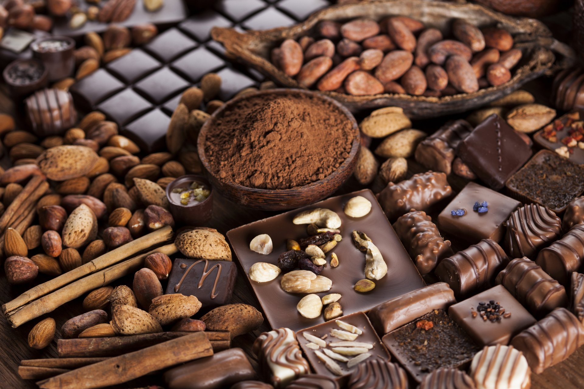 Close-up of assorted chocolate pieces, cocoa beans, cinnamon sticks, and cocoa powder, showcased in rich detail as a 4K Ultra HD desktop wallpaper of sweets and chocolate.