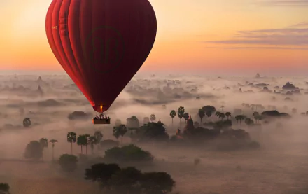 Hot air balloon floating over a foggy landscape during a sunrise, with the horizon and sky painted in warm hues. This HD desktop wallpaper captures a serene and breathtaking aerial view.