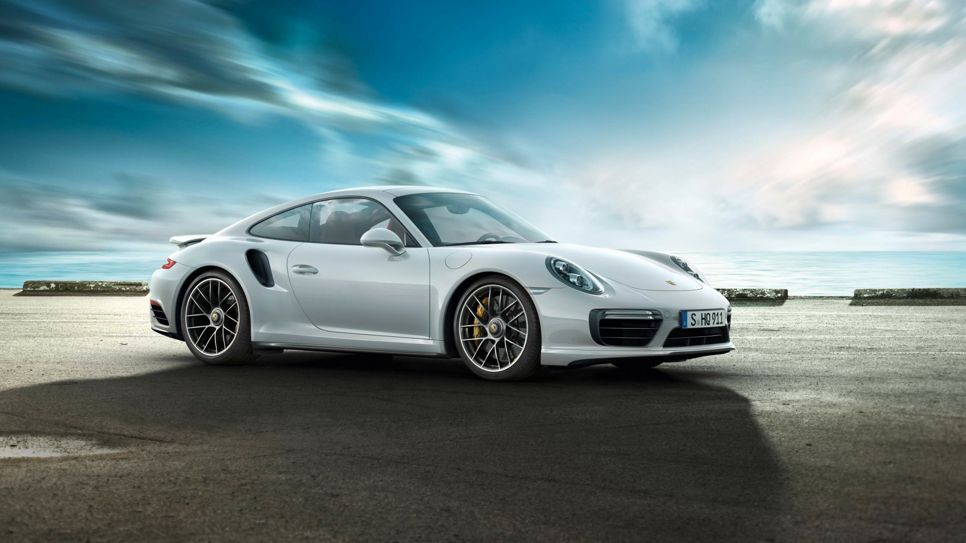 A white Porsche 911 Turbo parked on a paved surface under a cloudy sky, captured in high definition as a sleek automotive wallpaper background.