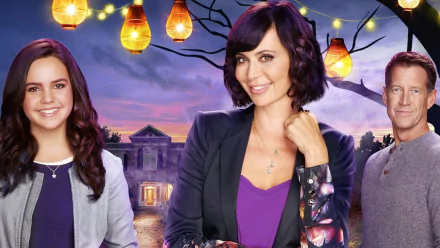 HD PC desktop wallpaper background of the TV show Good Witch: three characters smiling in front of a lit Victorian house at dusk with hanging lanterns and a purple sky.