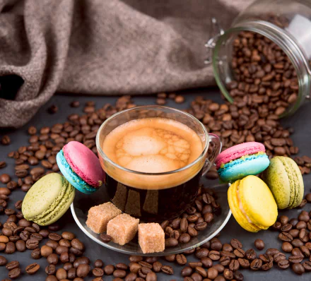 A vibrant still life featuring a cup of coffee surrounded by colorful macarons, sugar cubes, and scattered coffee beans, set against a cozy backdrop.