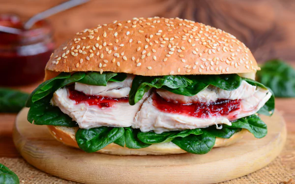 Close-up of a fresh burger with leafy greens and sliced turkey on a sesame seed bun, presented as a vibrant 4K Ultra HD PC desktop wallpaper.