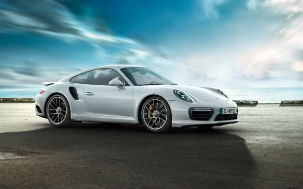 A white Porsche 911 Turbo parked on a paved surface under a cloudy sky, captured in high definition as a sleek automotive wallpaper background.