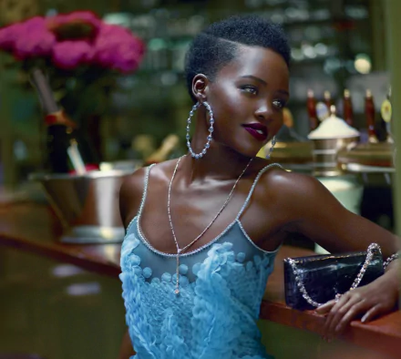 HD PC desktop wallpaper featuring celebrity Lupita Nyong'o in a stylish blue dress with large hoop earrings, posing confidently in a dimly lit setting.