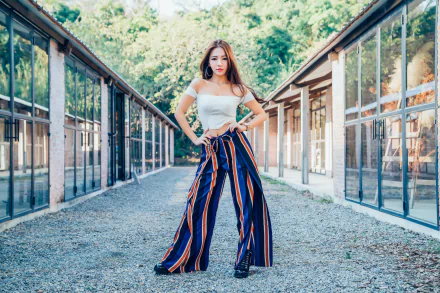 HD desktop wallpaper of an Asian brunette model wearing striped wide-leg pants and white top, standing confidently outdoors with lipstick accentuating her look.