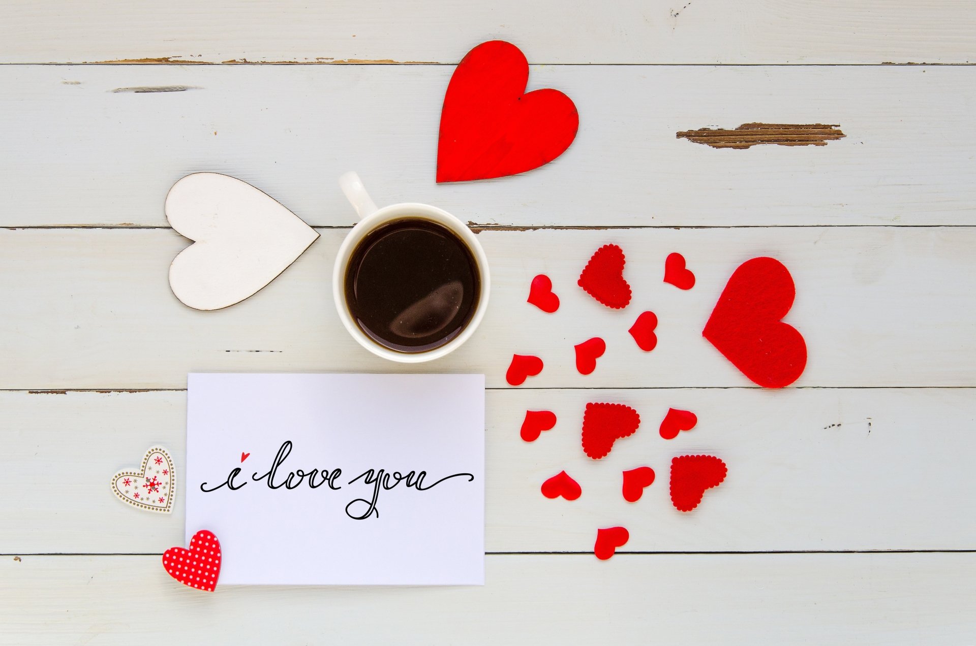 A romantic 4K Ultra HD wallpaper featuring a coffee cup, red and white hearts, and a handwritten i love you note on a white wooden background, evoking Valentine's Day love.