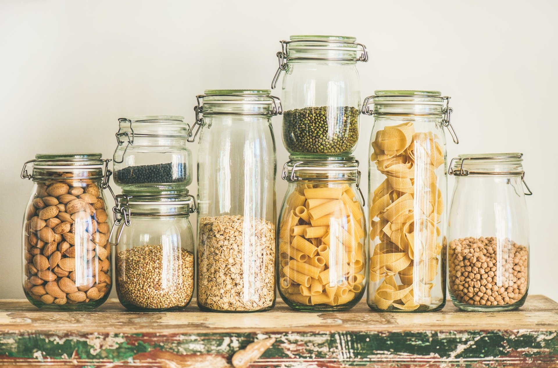 HD desktop wallpaper featuring a still life of glass jars filled with pasta, legumes, and grains, set against a neutral background on a rustic wooden surface.