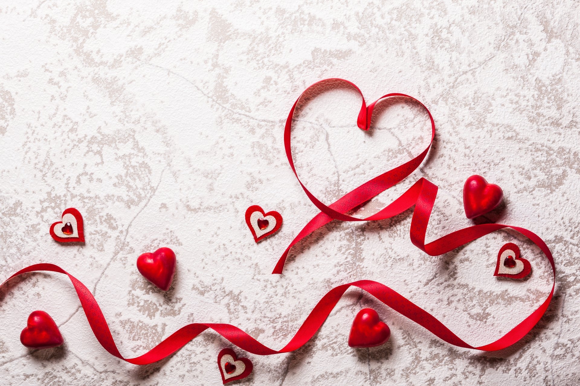 A red ribbon artistically shaped into a heart surrounded by small heart decorations on a light textured background, captured in 4K Ultra HD for PC desktop wallpaper.