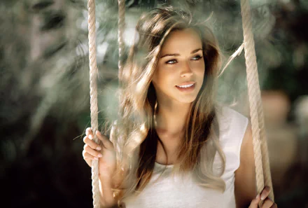 Brunette woman model with a soft smile sits on a swing, captured with shallow depth of field in a 4K Ultra HD desktop wallpaper background.