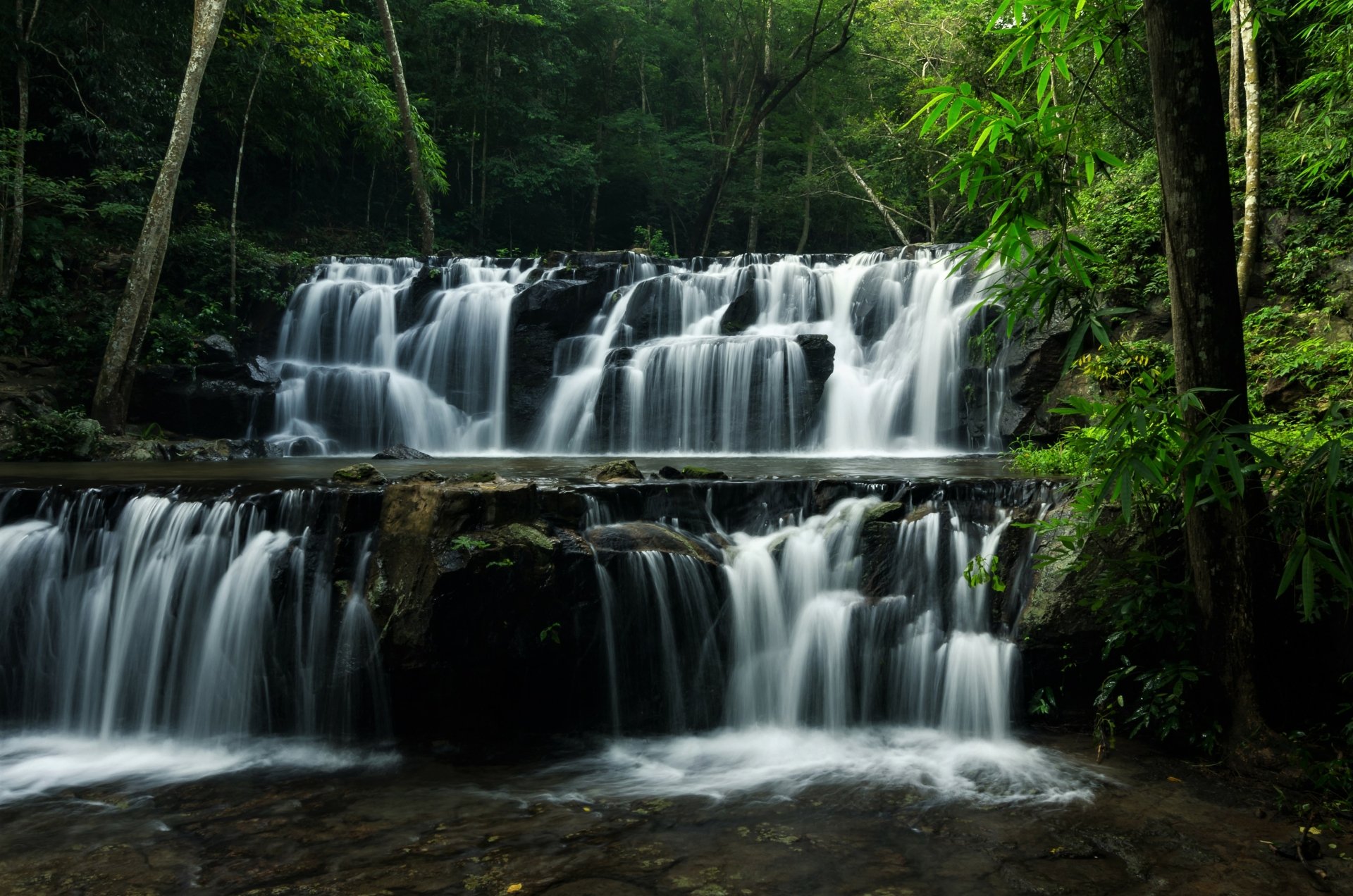 A serene 4K Ultra HD desktop wallpaper of a lush Thailand forest waterfall cascading over rocks surrounded by vibrant green foliage.