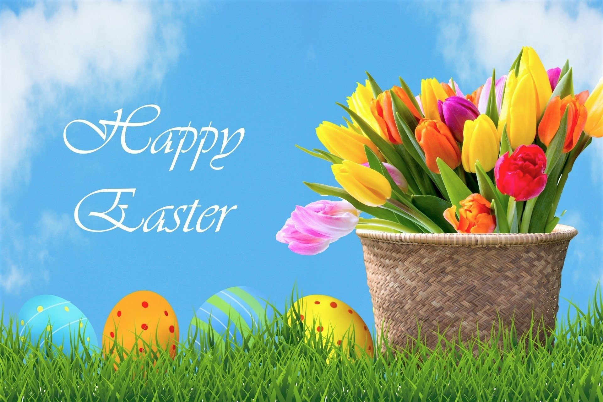 Colorful tulips in a basket with decorated Easter eggs on grass, set against a blue sky background with Happy Easter text, creating a vibrant holiday desktop wallpaper.