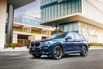 A blue BMW X3 SUV parked in front of modern glass buildings, showcased in a 4K Ultra HD PC desktop wallpaper and background.
