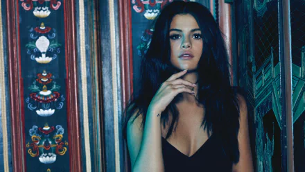 HD wallpaper of singer, actress, and model Selena Gomez with long black hair and brown eyes, standing against a decorative backdrop.