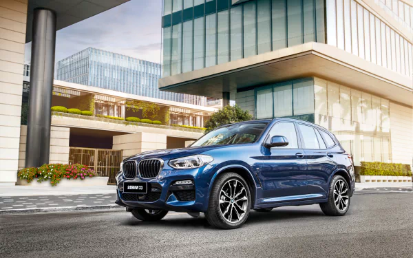 A blue BMW X3 SUV parked in front of modern glass buildings, showcased in a 4K Ultra HD PC desktop wallpaper and background.