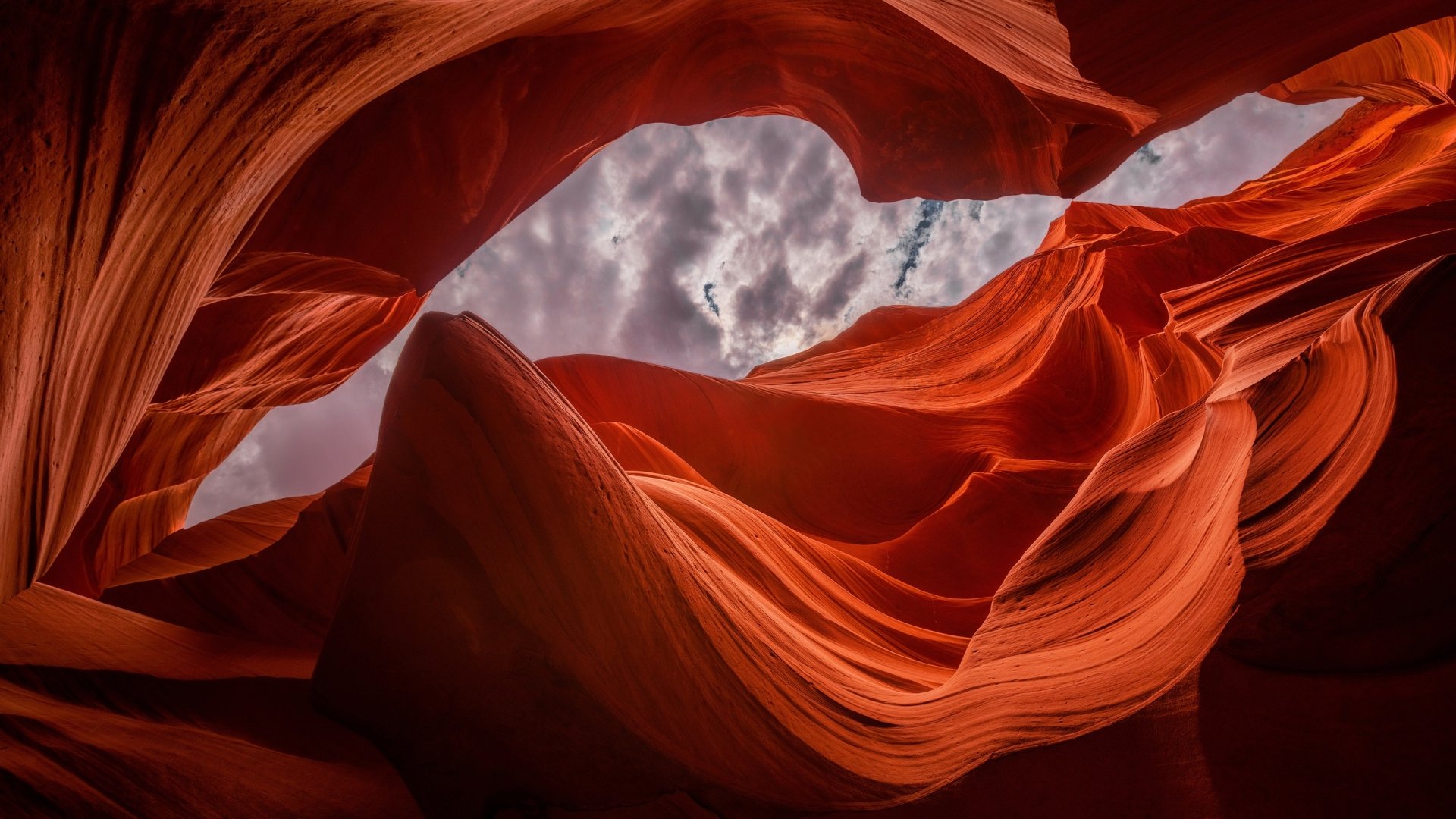 HD desktop wallpaper showcasing the striking natural curves and rich red hues of Antelope Canyon against a cloudy sky backdrop.