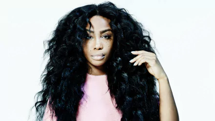 HD desktop wallpaper of SZA, featuring her with voluminous black hair and a pink top, posing against a white background.