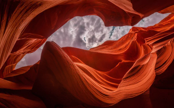 HD desktop wallpaper showcasing the striking natural curves and rich red hues of Antelope Canyon against a cloudy sky backdrop.