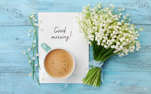 HD desktop wallpaper featuring a cup of coffee, a bouquet of white flowers, and a handwritten note saying Good morning! on a vibrant blue wooden surface, embodying a serene still life photography theme.