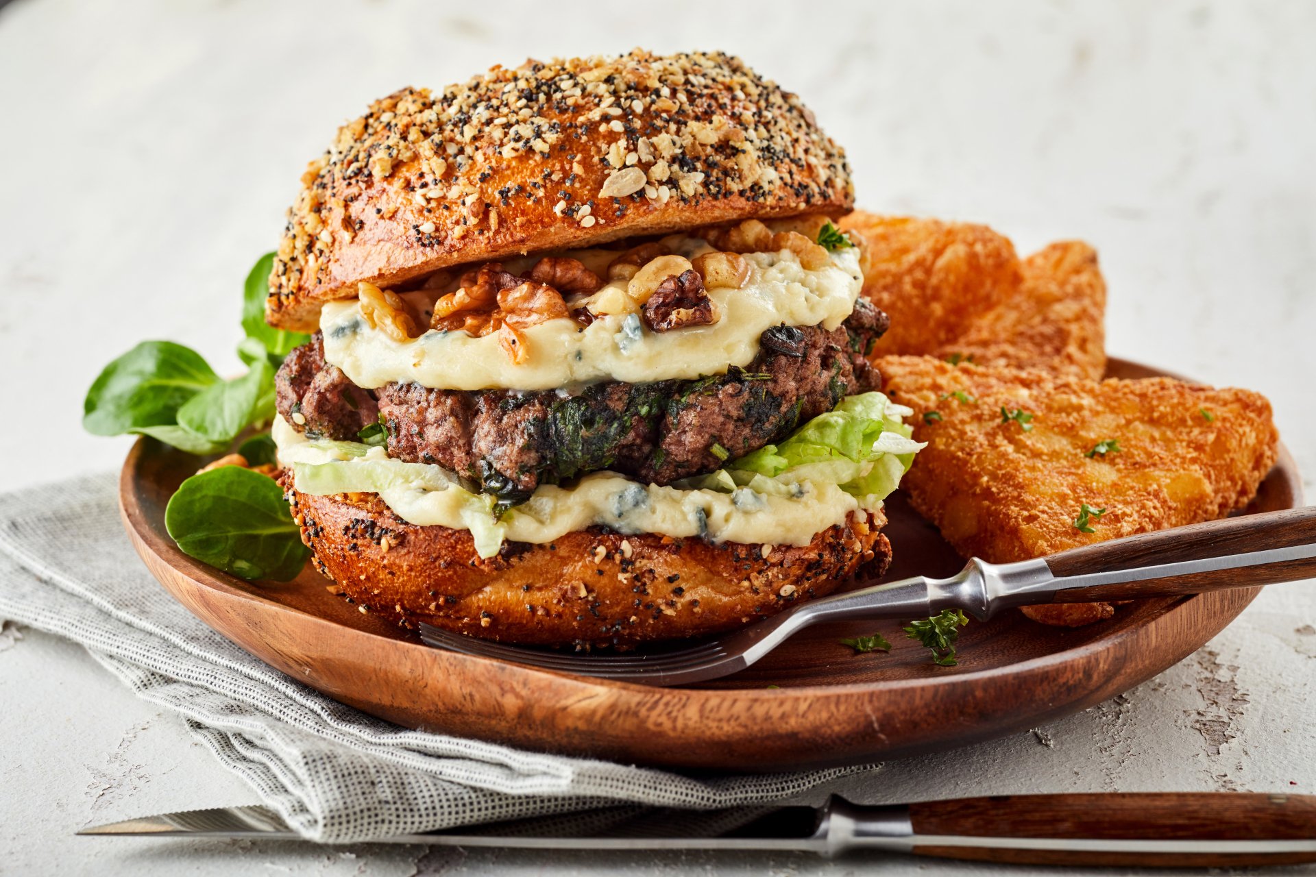 5K Ultra HD PC desktop wallpaper: food, burger — seeded bun stacked with a beef patty, melted cheese, greens and creamy slaw, served with crispy hash browns on a wooden plate.