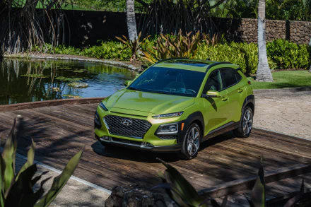 Green Hyundai Kona SUV parked near a pond with tropical plants in the background, shown as an HD PC desktop wallpaper and background.