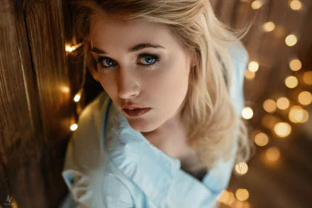 HD desktop wallpaper featuring a close-up of a blonde woman with blue eyes, softly illuminated by warm bokeh lights in the background.