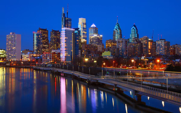 Nighttime view of Philadelphia skyline with illuminated skyscrapers reflecting on the river, showcasing the city's vibrant urban architecture in the USA.